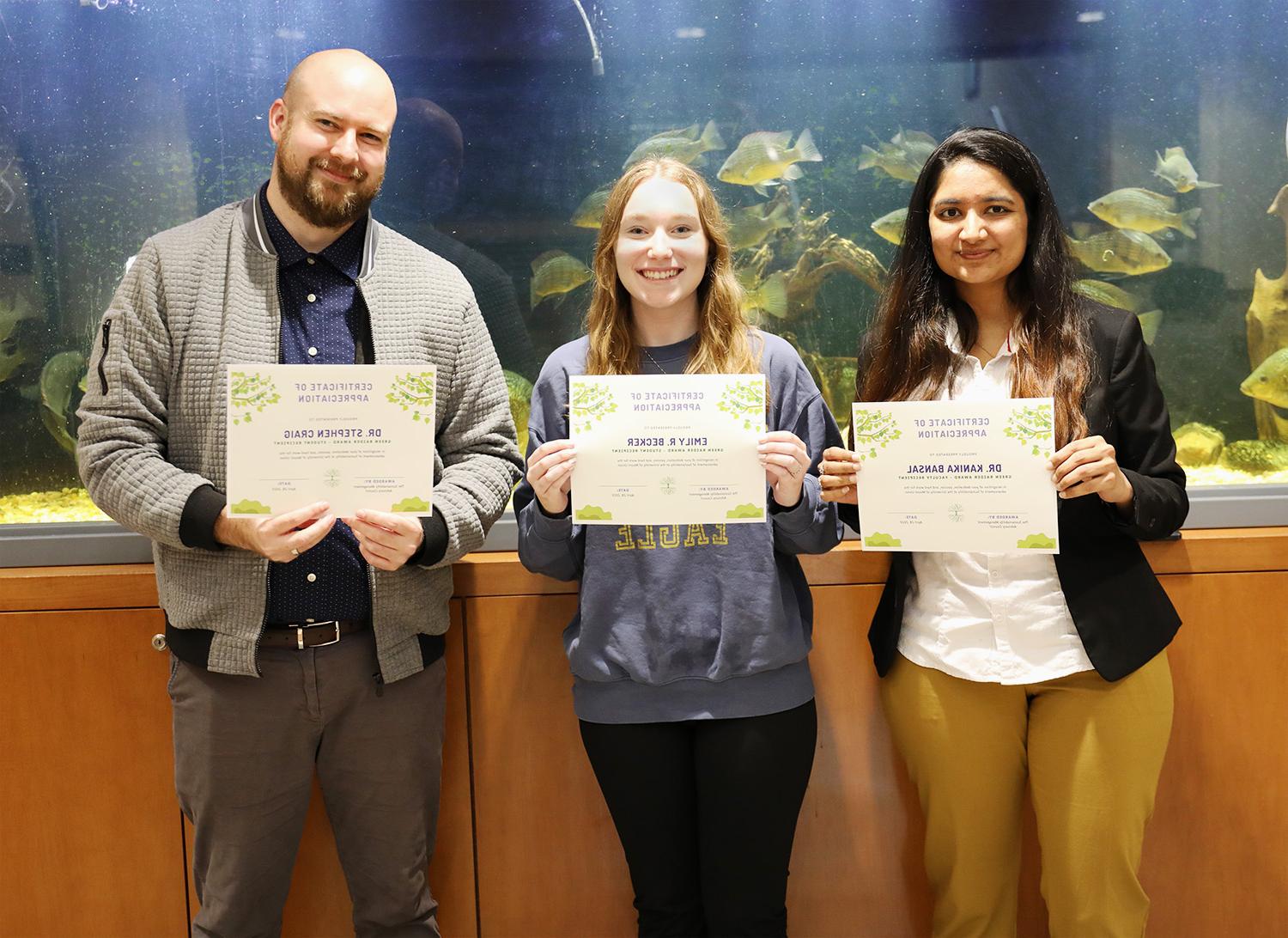 Three Green Raider Award recipients stand in front of a fish tank smiling while holding their award certificates